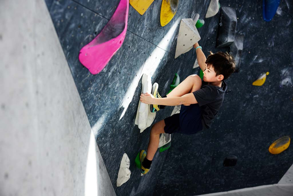 Junge im schwarzen Oberteil an der Boulderwand