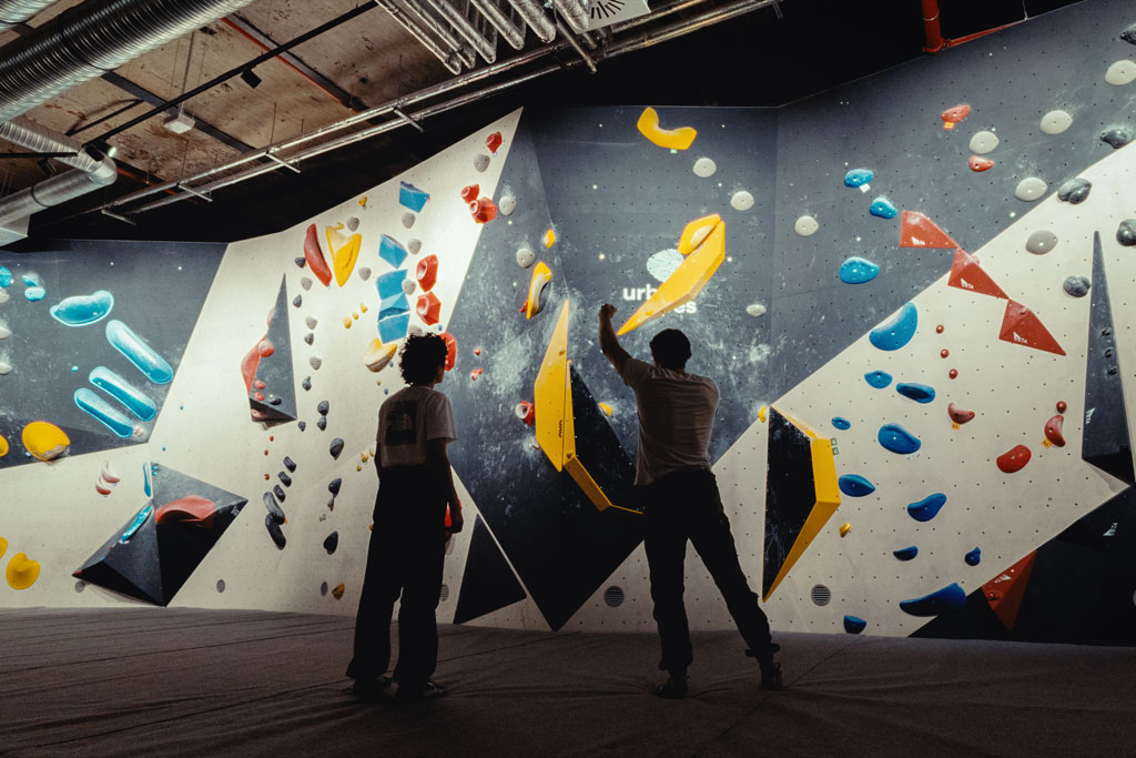 Zwei Personen betrachten Boulderwand im urban apes Fhain Berlin und planen ihren nächsten Zug.